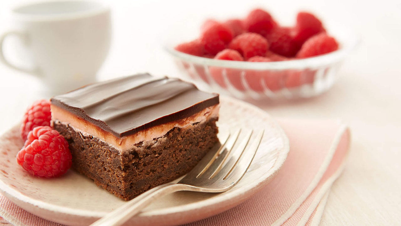 serving dish topped with chocolate raspberry dessert beside bowl of fresh raspberries